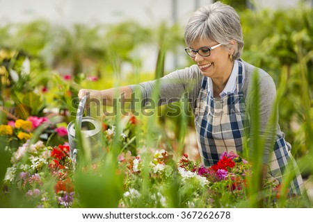 Beautiful mature woman in a garden watering flowers