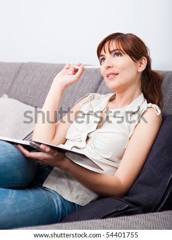 Woman thinking sitting on couch holding a pen and a book