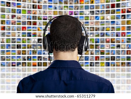 Back view of a young man with head phones watching a big TV panel