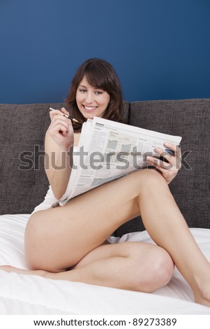 Happy young woman lying on the bed and seek for a job on the newspaper