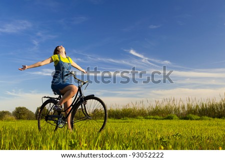 Happy girl over a bicycle and looking the view, in a green meadow