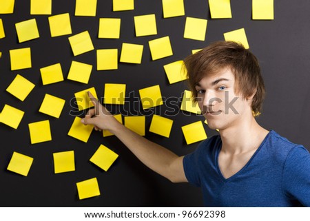 Young student pointing to a board full of yellow notes and looking in to the camera