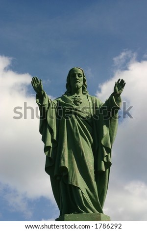 A statue of jesus blessing, against a blue sky with some small white clouds