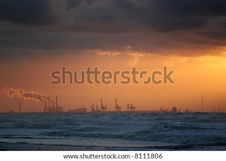 Sunset at sea, with smoking chimneys and oil industry in the background.