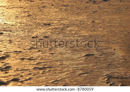 The beach is left covered with a thin layer of water and foam in the soft light of evening.