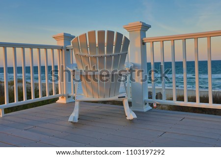 Adirondack chair sitting on a deck balcony overlooking the ocean and beach at sunset.  This location is in the Outer Banks of North Carolina.