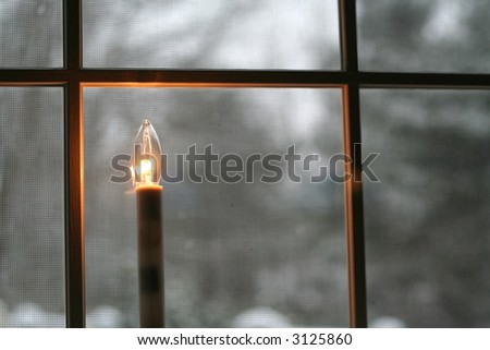 welcoming Christmas candle burns in the window looking out to a fresh snowfall