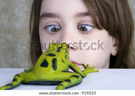 A little girl looks cross-eyed at her pet rubber frog.