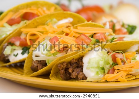 A plate of freshly prepared ground beef tacos, with tomato, freshly grated cheese, lettuce and sour cream.