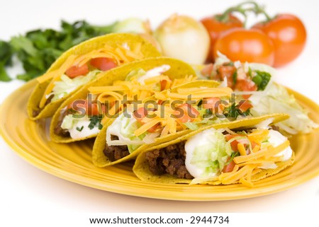 A whole plate of ground beef tacos. Fresh ingredients are shown in the background. Selective focus.