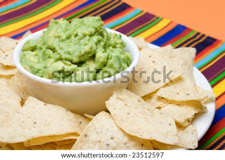 A bowl of freshly made guacamole, surrounded by fresh corn tortilla chips. Colorful background.