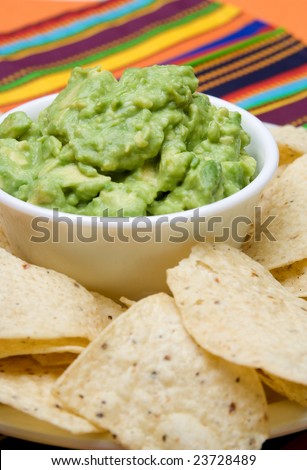 A bowl of fresh guacamole and corn tortilla chips on a colorful background.