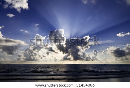 Sunrise over large body of water with rays of light coming through clouds