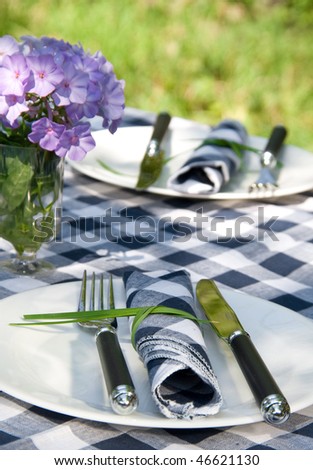 The table with cheked table-cloth and two served plates in the garden