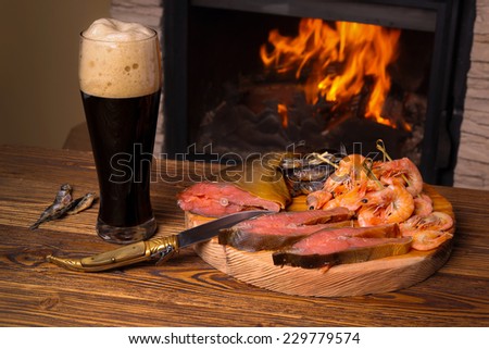 Glass of dark beer and a tray of assorted fish on a background of a burning fireplace