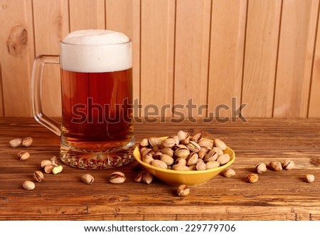 Mug with light beer and pistachios on wooden table