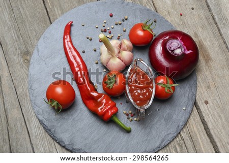 Ketchup chili in a glass gravy boat and its ingredients on a black tray