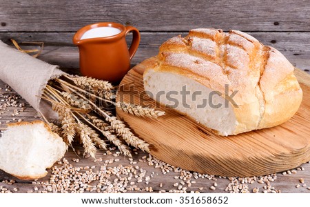 Homemade bread, milk and ripe ears of rye on a wooden background, place for text