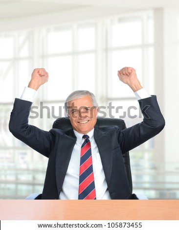 Businessman seated at his office desk with his fists in the air to celebrating a closed deal.