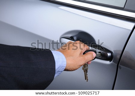 Closeup of a man\'s hand inserting a key into the door lock of a car. Horizontal format. Car and man are unrecognizable.