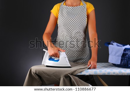 Closeup of a woman ironing clothes. Horizontal format over light to dark gray background. Woman is unrecognizable.