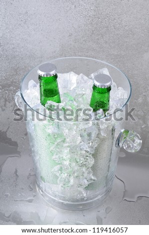 Two green beer bottles in a crystal ice bucket sitting on a wet stainless steel surface.