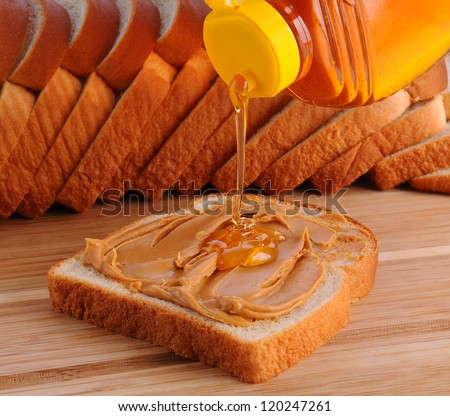 Closeup of making a peanut butter and honey sandwich. Shallow Depth of field with slices of bread in the background.