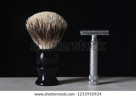 Mens Razor and Shaving Brush: Two mens grooming aids on a bathroom counter top. Items are covered with water droplets against a black background.