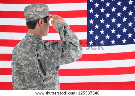 Closeup of a young American Soldier in Fatigues saluting the Flag. Flag fills the frame and is out of focus. Man is seen from behind.