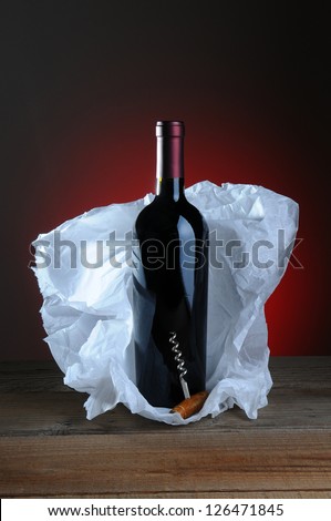 Red Wine Bottle and Cork Screw with tissue paper wrapping on wood surface and light to dark background.
