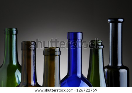 Closeup of a group of empty wine bottles over a light to dark gray background.