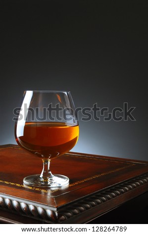 Closeup of a brandy snifter on a fancy antique wooden table with a light ot dark gray background. Vertical format with copy space.