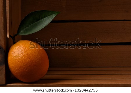 Closeup of a fresh picked navel orange in a wood packing crate. The lone fruit has a stem and leaf and is leaning on the side of the box.