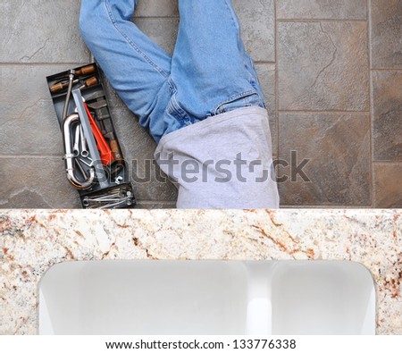 High angle view of a plumber laying under a kitchen sink. Man is unrecognizable with a tool box next to him.
