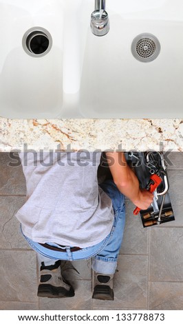 High angle view of a plumber under a kitchen sink reaching for a wrench from the tool box next to him. Man is unrecognizable. Vertical Format.