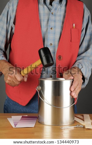 Paint store employee pounding down the lid of a paint can. Horizontal format, with paint chips, opener and stir sticks on the counter. Man is unrecognizable.