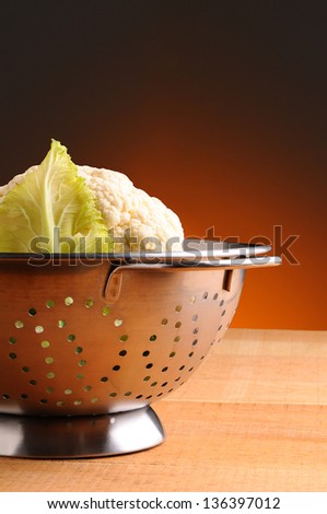 Fresh picked cauliflower in a metal colander on rustic wooden table. Vertical format with a light to dark warm background.