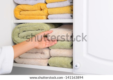 Closeup of a womans hand taking a towel from a linen closet. Arm is partially covered by her bathrobe. Horizontal format.