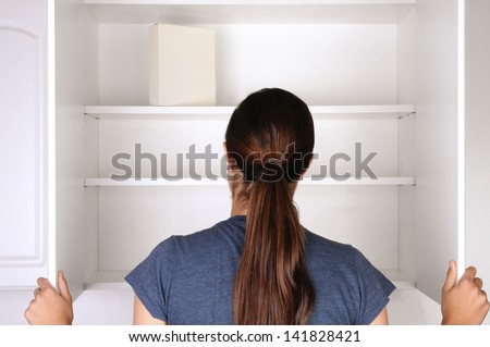 Closeup of a woman looking in an empty pantry. Seen from behind there is only one box of food. Horizontal format.