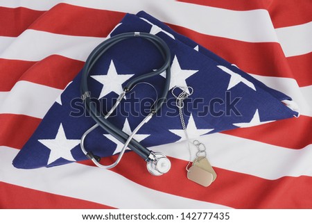 A stethoscope and dog tags on a folded American Flag. The background is the red and white stripes of another flag. Ideal for Military Health care concepts.