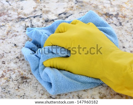 Closeup of a hand in a yellow latex glove using a blue towel to clean a counter top.