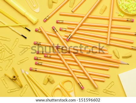 School supplies. Pencils, erasers, paper clips, brushes, pins, scissors, paper laying in a random pattern on a yellow background. Everything in a shade of yellow..