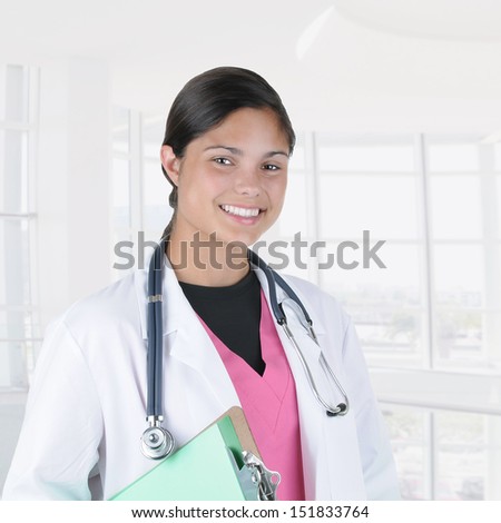 Closeup of a female nurse or doctor Inside a modern medical facility. The woman is wearing a lab coat and surgical scrubs while smiling at the camera.