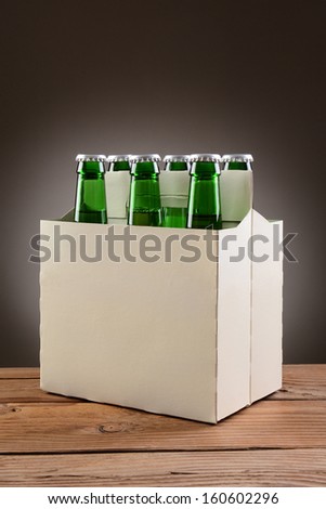 Closeup of a six pack of green beer bottles on a rustic wooden table. Vertical format with a light to dark gray spot background.