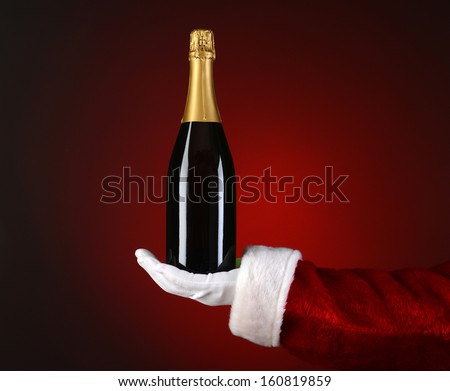 Closeup Of Santa Claus Holding A Bottle Of Champagne In The Palm Of His Outstretched Hand. Hand And Arm Only Over A Light To Dark Red Spot Background.