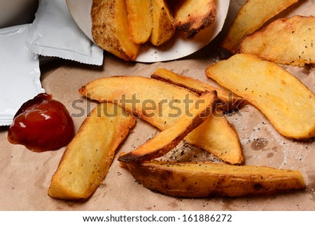 Closeup of  some French Fries spilled onto a brown bag. Ketchup dollop and packets  with salt and pepper. Horizontal format filling the frame.