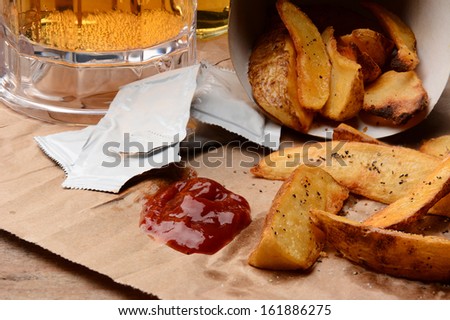 French Fries spilled onto a brown bag. Ketchup dollop and packets  with salt and pepper and mug of beer. Horizontal format filling the frame.