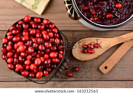 Overhead of a bucket of cranberries and a pot full of whole cranberry sauce on a rustic wooden table. Cranberry sauce is a traditional Thanksgiving side dish. Horizontal format.
