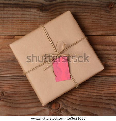 Overhead view of a single holiday package wrapped with eco friendly craft paper and tied with twine. Square format on a rustic wooden table.