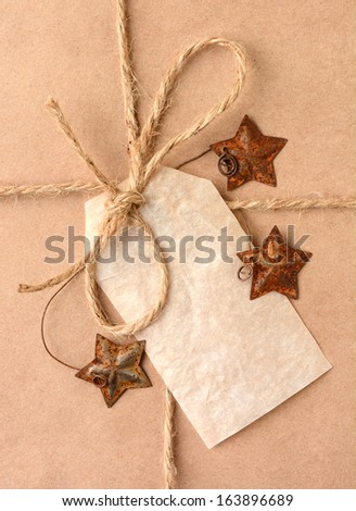 Closeup of a gift tag on a Christmas present. The package is wrapped in plain brown paper with a tied with twine. The package is adorned with metal star shaped ornaments. Vertical Format.